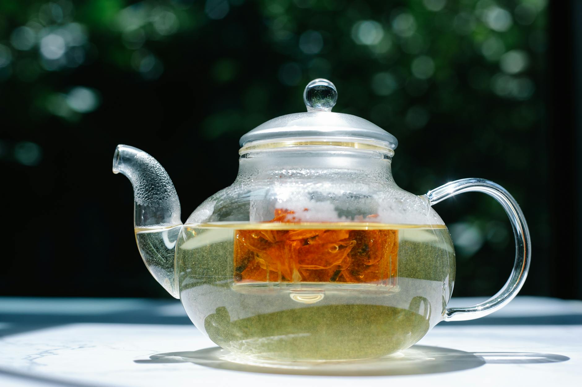 Tetera de vidrio con té y hojas en infusión.